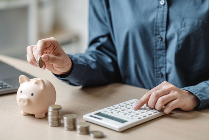 Mercado Pago: mãos digitando em calculadora e colocando moedas em um cofrinho para administrar a receita previsível da empresa