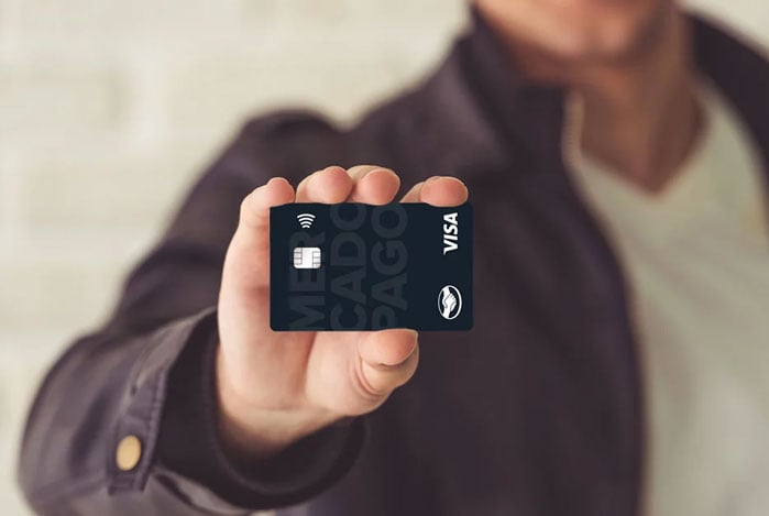 Mãos de um homem segurando o cartão Mercado Pago que será usado para fazer as compras de fim de ano de forma equilibrada e com segurança.