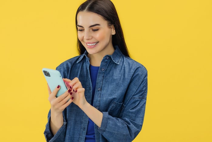 Mulher vestindo blusa azul com uma camisa jeans por cima, mexendo no celular para aprender como usar a Linha de Crédito Mercado Pago