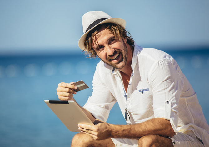 Homem vestindo camisa branca, shorts branco e chapéu, sentado com um tablet em uma das suas mãos e na outra o cartão, ele busca aprender como usar o cartão de crédito com ajuda do banco digital Mercado Pago