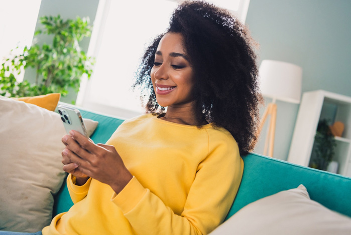 Mercado Pago: mulher sentada no sofá, sorrindo e mexendo no celular com a tranquilidade de quem sabe como usar a Linha de Crédito Mercado Pago